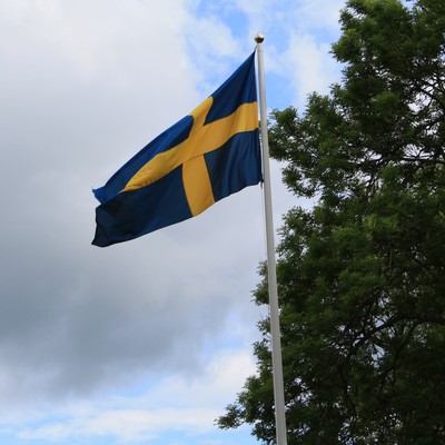 Den svenska flaggan vajar för vinden med en klarblå himmel i bakgrunden.